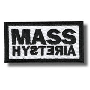 Peut inclure: Un écusson rectangulaire avec l'inscription "MASS HYSTERIA" en lettres noires grasses sur fond blanc. Le patch est bordé d'un liseré noir cousu.