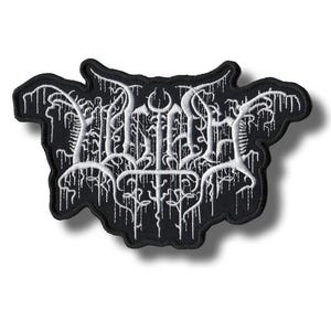 Può includere: Toppa nera con testo bianco stilizzato. Il testo ha un'estetica gotica o metal, con dettagli intricati e gocciolanti. La toppa ha una forma irregolare unica ed è probabilmente un emblema o un logo.