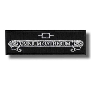 Puede incluir: Parche rectangular negro con texto bordado blanco y elementos decorativos. El texto dice "OMNIUM GATHERUM" en una fuente estilizada, con un pequeño diseño geométrico encima. El parche tiene un diseño limpio y minimalista.
