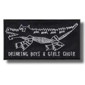 Può includere: Toppa rettangolare nera con un'illustrazione di dinosauro ricamata in bianco e la scritta "DRINKING BOYS & GIRLS CHOIR". Il dinosauro è stilizzato con linee frastagliate.