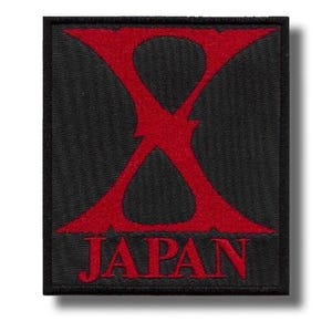 Może przedstawiać: Czarna kwadratowa naszywka z dużym czerwonym wzorem "X" i napisem "JAPAN" w kolorze czerwonym. Naszywka ma czarną obwódkę i prawdopodobnie jest haftowana lub tkana.