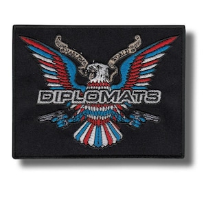 May include: Black embroidered patch with a design of an eagle with red, white, and blue wings, holding two pistols. The word "DIPLOMATS" is in white block letters. The patch also includes the text "HARLEM WORLD" in a banner.