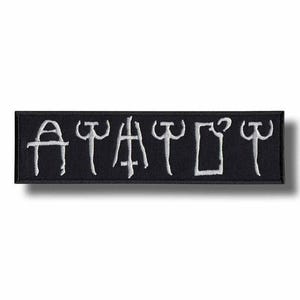 Peut inclure: Écusson rectangulaire noir avec texte brodé blanc. Le texte est dans une police stylisée, peut-être un symbole ou un mot. L'écusson a une bordure noire et est probablement en tissu.