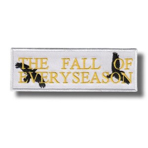 May include: Rectangular white patch with gold embroidered text and black bird silhouettes. The text reads "THE FALL OF EVERYSEASON". The patch has a white border and is likely an iron-on patch or sew-on patch.