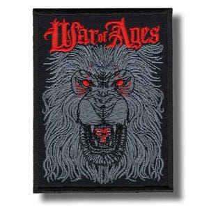 May include: Embroidered patch with a snarling lion's head, red eyes and teeth. The text "War of Ages" is arched above the lion in red. The patch is rectangular with a black border and background.
