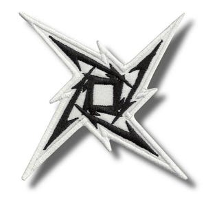 May include: Embroidered patch featuring a black and white design. The patch has a starburst shape with sharp points and a central square design. The edges are white with black detailing, creating a striking contrast. The patch is likely for clothing or accessories.