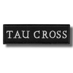 Puede incluir: Parche rectangular negro con el texto bordado "TAU CROSS" en blanco. El parche tiene un borde negro y está diseñado para ser cosido o planchado sobre tela. El diseño es sencillo y el texto es claro.
