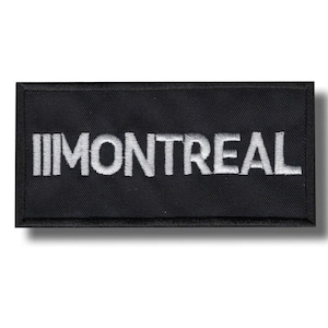 Op de afbeelding: Zwart rechthoekig embleem met het woord "MONTREAL" in het wit geborduurd. De patch heeft een zwarte rand en is waarschijnlijk een embleem of logo.