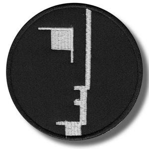 May include: Black circular patch with a white geometric design. The design features a vertical line with horizontal and angled lines. The patch has a black border and a white stitched design.