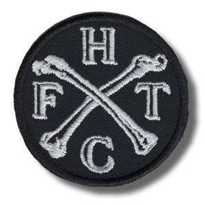 May include: Black circular patch with white embroidered text and crossed bones. The letters "H", "F", "T", and "C" are embroidered around the crossed bones. The patch has a black border.