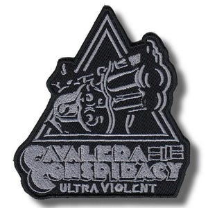 Può includere: Toppa ricamata nera e grigia con la scritta "CAVALERA CONSPIRACY" e "ULTRA VIOLENT". La toppa presenta un design triangolare con un'illustrazione stilizzata di una figura e di una motocicletta.