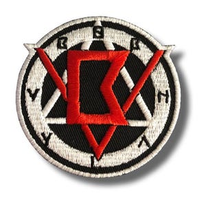 Op de afbeelding: Ronde geborduurde patch met een zwarte achtergrond en een witte rand. De patch heeft een rood geometrisch ontwerp in het midden, met witte driehoeken en letters langs de rand. De patch heeft een witte rand en is waarschijnlijk voor kleding of accessoires.