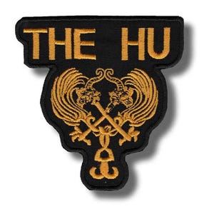 Può includere: Toppa ricamata nera con la scritta "THE HU" in oro. La toppa presenta un elaborato disegno dorato di due spade incrociate con teste di drago e ali ornate. La toppa ha una forma unica.