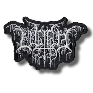 Puede incluir: Parche bordado en blanco y negro con texto estilizado. El parche tiene una forma única con un borde negro y detalles blancos en forma de goteo. El texto parece ser un logotipo o emblema de una banda.