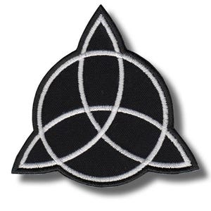 May include: Black patch with a white Celtic knot design, or triquetra, in a triangular shape. The patch has a white border and is likely for clothing or accessories.