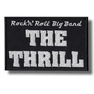 Op de afbeelding: Zwart rechthoekig embleem met wit geborduurde tekst. De tekst luidt bovenaan "Rockin' Roll Big Band", in het midden "THE" en onderaan "THRILL". Het embleem heeft een zwarte rand.