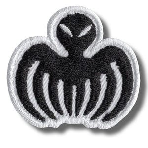 May include: Embroidered patch with a black alien-like design, white detailing, and a white border. The symmetrical shape features curved lines and a stylized head. Suitable for application on clothing or accessories.