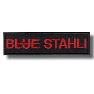 Könnte beinhalten: Ein rechteckiger, schwarzer, gestickter Aufnäher mit den Worten "BLUE STAHLI" in roter Farbe. Der Text ist mittig auf dem Aufnäher platziert, mit einem stilisierten "U" in "BLUE". Der Aufnäher hat ein sauberes, professionelles Aussehen.