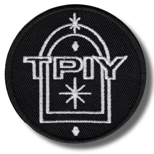 Könnte beinhalten: Ein runder, schwarzer, gestickter Aufnäher mit weißem Text und Design. Der Text "TPY" ist in einem Quadrat zentriert, mit einem bogenförmigen Design darüber und einem Stern darunter. Zusätzliche Sternausbrüche und Punkte vervollständigen das Design.