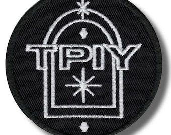 May include: A round, black embroidered patch with white text and design. The text "TPY" is centered within a square, with an arched design above and a starburst below. Additional starbursts and dots complete the design.