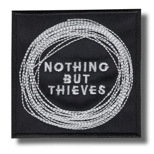 Pode incluir: Patch quadrado preto com texto e design bordados em branco. O texto diz "NOTHING BUT THIEVES" em letras maiúsculas. Um design circular de fio branco envolve o texto. O patch tem uma borda preta.