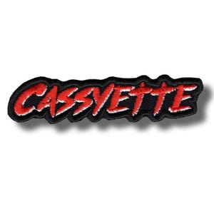 Puede incluir: Parche bordado con la palabra "CASSVETTE" en rojo, contorneada en blanco, sobre un fondo negro. El parche tiene forma rectangular con esquinas redondeadas. El texto está en una fuente audaz y estilizada.