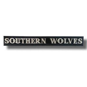 May include: A black rectangular sign with the words "SOUTHERN WOLVES" in a stylized, light-colored font. The text is centered on the sign, which appears to be made of a dark material.