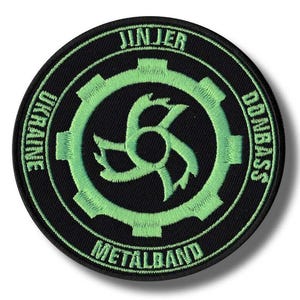 May include: A round black patch with green embroidered text and design. The text reads "JINJER", "UKRAINE", "DONBASS", and "METALBAND". The central design is a stylized gear with a unique symbol.