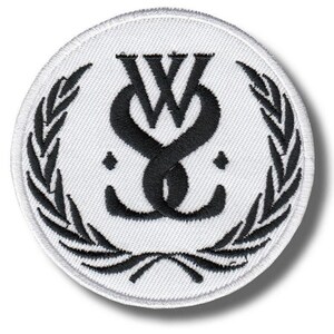 Może przedstawiać: Okrągła, biała naszywka z czarnym, przeplatanym wzorem "W" i "S". Emblemat otoczony jest czarnym wieńcem laurowym. Naszywka ma białą obwódkę.