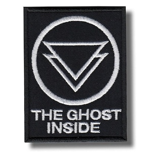 Op de afbeelding: Zwart rechthoekig embleem met wit geborduurd ontwerp. Het ontwerp toont een cirkel rond twee overlappende driehoeken, met de tekst "THE GHOST INSIDE" eronder. Het embleem heeft een zwarte rand en is waarschijnlijk voor kleding of accessoires.