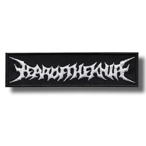 Puede incluir: Un parche rectangular negro con texto bordado en blanco "BEARD OF THE KNIFE" en una fuente gótica estilizada. El parche está diseñado para ser cosido en ropa o accesorios. El texto tiene un borde blanco.