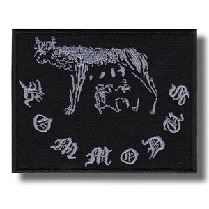 Peut inclure: Écusson carré noir avec une illustration argentée détaillée d'un loup et de deux petites figures. Le motif est entouré de texte stylisé. L'écusson a une bordure noire et un effet d'ombre.