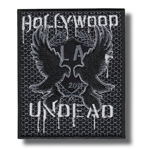 May include: A black and gray embroidered patch featuring the text "HOLLYWOOD UNDEAD" with dripping font. The patch has a central emblem with "LA" and "2018" and two stylized bird wings.
