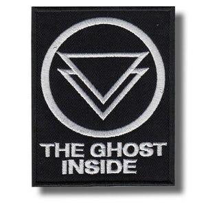 Op de afbeelding: Zwart rechthoekig embleem met wit geborduurd ontwerp. Het ontwerp toont een cirkel met twee overlappende omgekeerde driehoeken. De tekst "THE GHOST INSIDE" is eronder geborduurd.