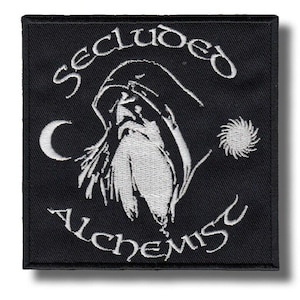 Pode incluir: Patch quadrado preto com texto e imagens bordadas em branco. O texto diz "Secluded Alchemist" acima e abaixo de uma figura encapuzada com uma longa barba. Uma lua crescente e uma explosão solar estão em ambos os lados da figura.