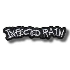 Op de afbeelding: Een zwart geborduurd embleem met de tekst "INFECTED RAIN" in witte, gestileerde letters. Het embleem heeft een zwarte rand en is waarschijnlijk bedoeld om op kleding of accessoires te naaien of te strijken. De algehele uitstraling is edgy en opvallend.
