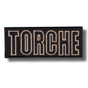 Könnte beinhalten: Schwarzer rechteckiger Aufnäher mit dem Wort "TORCHE" in beigen Blockbuchstaben gestickt. Der Aufnäher hat einen schwarzen Rand und einen Schatteneffekt.