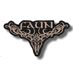 Puede incluir: Parche bordado negro con la palabra "FAUN" en hilo color beige. El parche tiene un diseño decorativo y simétrico con patrones arremolinados y una forma estilizada que se asemeja a una cabeza de animal.