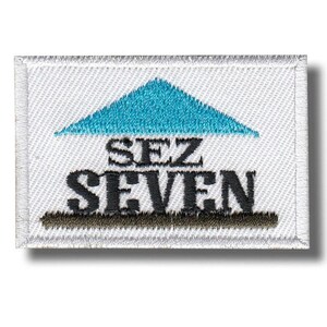 Peut inclure: Écusson brodé rectangulaire avec le texte "SEZ SEVEN" en noir, sous un triangle turquoise. Le patch a un fond blanc et une bordure cousue.