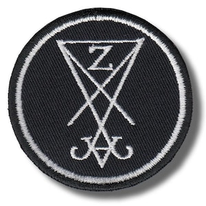 Op de afbeelding: Ronde zwarte patch met een wit geborduurd ontwerp. Het ontwerp toont een driehoek met de letter "Z" erin, gekruiste lijnen en een gestileerd symbool aan de onderkant. De patch heeft een witte rand.