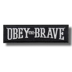 Könnte beinhalten: Schwarzer rechteckiger Aufnäher mit weiß gesticktem Text "OBEY THE BRAVE". Der Aufnäher hat einen schwarzen Rand und einen Schatteneffekt. Der Text ist in einer fetten, stilisierten Schriftart gehalten.