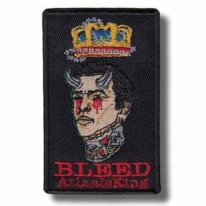 Może przedstawiać: Czarna prostokątna naszywka z wystylizowaną ilustracją osoby z rogami diabła, koroną i czerwonymi łzami. Tekst "BLEED AtlasKing" jest czerwony. Naszywka ma szczegółowy haftowany wzór.