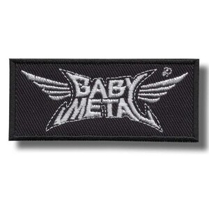 以下が含まれることがあります： 黒い長方形のパッチ。白い文字で「BABY METAL」と書かれており、翼と鋭い角度でデザインされています。織り込まれた質感のこのパッチは、衣類やアクセサリーへの使用を目的としている可能性があります。
