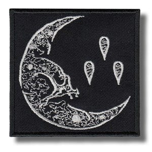 以下が含まれることがあります： 黒い正方形のパッチ。白い刺繍の三日月と3つの白い涙の形が特徴です。月のデザインは詳細な刺繍が施されています。パッチには黒い縁取りと影があります。