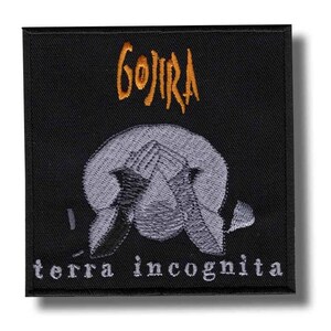 以下が含まれることがあります： オレンジ色の「GOJIRA」の文字と灰色のイラスト、白い文字で「terra incognita」が描かれた黒い正方形のパッチ。バンドや音楽グッズ用のパッチである可能性が高いです。