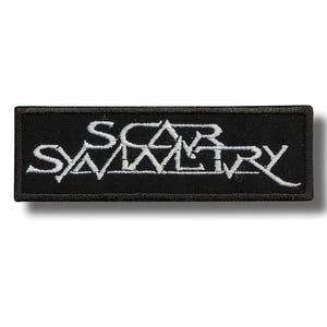 Puede incluir: Parche rectangular negro con el texto blanco "SCAR SYMMETRY". El texto está en una fuente estilizada. El parche tiene un borde negro, probablemente un parche bordado.