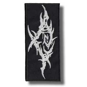 May include: Black rectangular patch with a white, abstract design. The embroidered design features sharp, angular shapes. The patch is likely for clothing or accessories, and is a decorative item.
