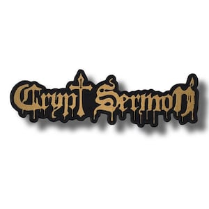 Może przedstawiać: Czarna i złota naszywka z napisem "Crypt Sermon" w gotyckiej czcionce. Naszywka posiada krzyż i efekt kapania, idealna na odzież lub akcesoria.