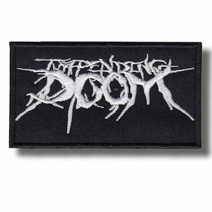 May include: Black rectangular patch with white embroidered text that reads "Impending Doom" in a stylized, gothic font. The patch has a black border and is likely designed to be sewn onto clothing or accessories.