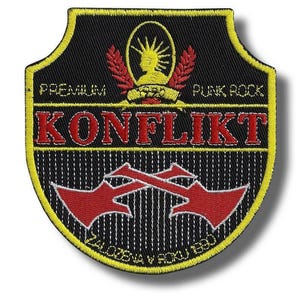 Może przedstawiać: Czarna i żółta haftowana naszywka z czerwonym napisem "KONFLIKT", o tematyce punk rock. Naszywka zawiera tekst "PREMIUM PUNK ROCK" i "ZALOZENA V ROKU 1990".